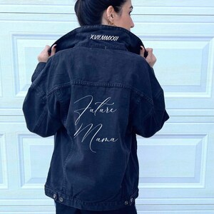 Pu&ograve; includere: Giacca di jeans nera con ricamo bianco che dice "Future Mama" sul retro. Il colletto &egrave; ricamato con la data in numeri romani "XVII.MMXXII".