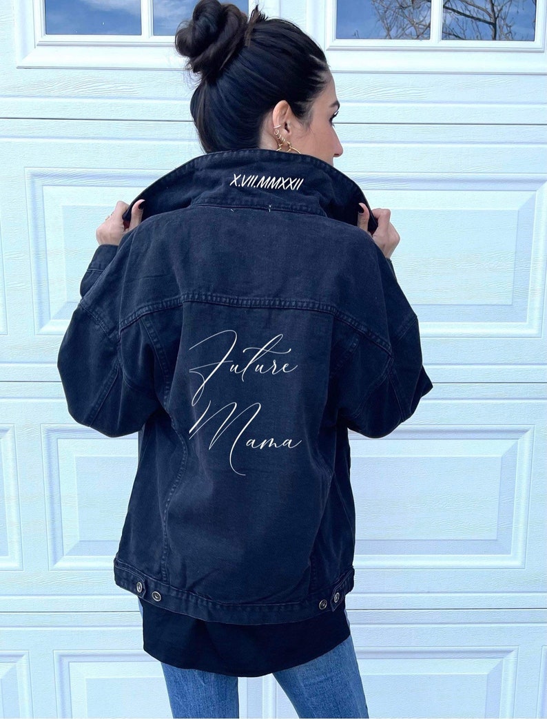 Pu&ograve; includere: Giacca di jeans nera con ricamo bianco che dice "Future Mama" sul retro. Il colletto &egrave; ricamato con la data in numeri romani "XVII.MMXXII".
