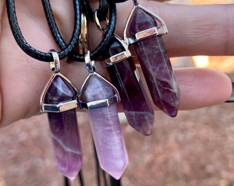 May include: Five amethyst crystal point pendants on black cords. The pendants are silver-toned and have a faceted design.