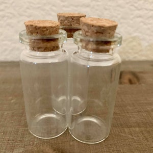 Può includere: Tre piccole bottiglie di vetro con tappi di sughero. Le bottiglie sono trasparenti e hanno una forma rotonda.