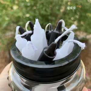 Pode incluir: Um frasco de vidro cheio de velas de chá brancas e pretas. O frasco tem uma tampa preta.