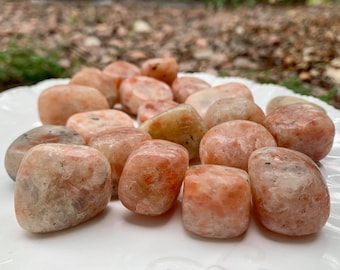 May include: A collection of tumbled sunstone stones in various shades of orange, white, and brown. The stones are smooth and polished, with a natural, earthy look.