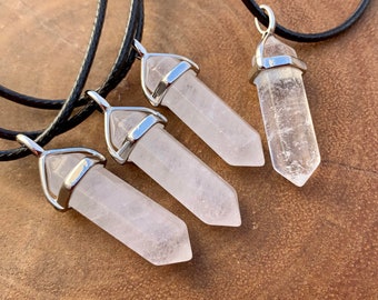 May include: Four crystal pendant necklaces. Three pendants are a light pink color, and one is clear. Each crystal is mounted in a silver-colored metal setting and hangs from a black cord.