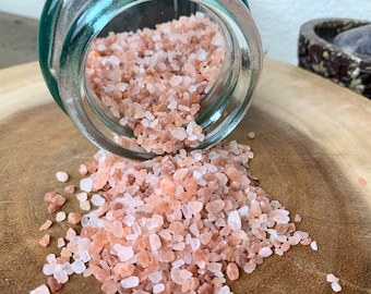 May include: Pink Himalayan salt crystals spilling out of a clear glass jar onto a wooden surface.