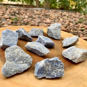 May include: A collection of blue kyanite crystal roughs. The crystals are various sizes and shapes, with a light blue color and a rough, natural texture.