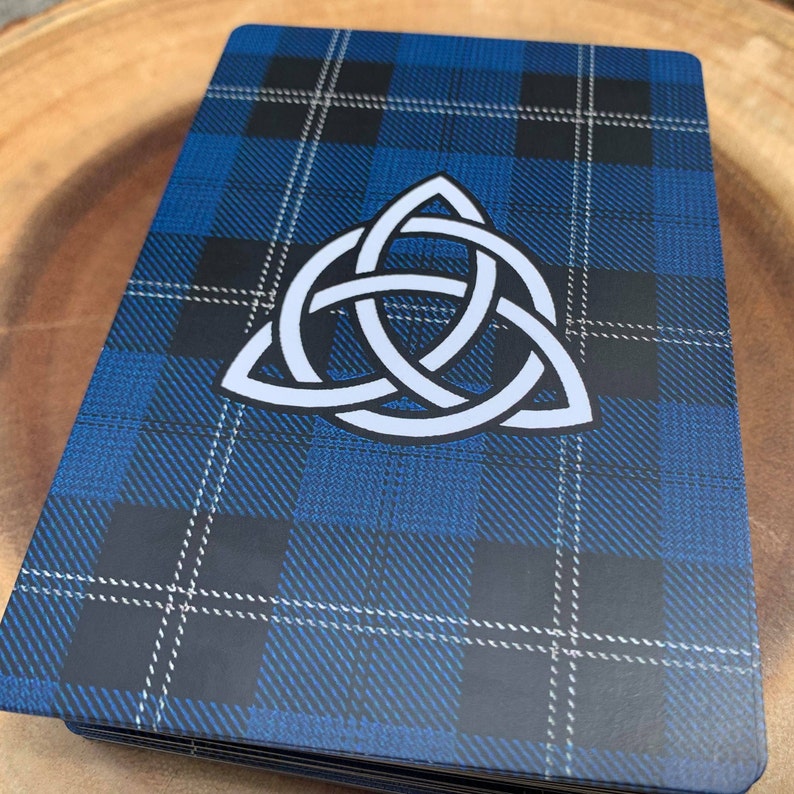 May include: A blue and black tartan background with a white Celtic knot design in the centre.