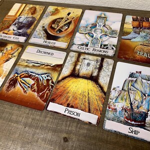May include: A set of nine tarot cards with colourful illustrations and text. The cards include "Modern Era", "Healer", "Celtic Regions", "Trauma", "Drowned", "Prison", "Ship", "Burned", and "The Fool".