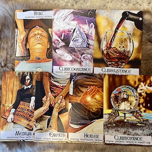 May include: A set of ten tarot cards with colorful illustrations and text. The cards are arranged in two rows of five. The top row features cards titled "Reiki", "Claircognizance", "Clairgustance", "Empath", and "Healer". The bottom row features cards titled "Medium", "Clairvoyance", "The World", "The Sun", and "The Moon".