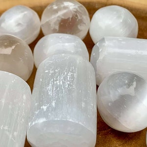 May include: A collection of white selenite crystals in various shapes, including spheres and cylindrical forms. The crystals have a translucent appearance and a smooth, polished surface. The arrangement showcases the natural beauty of the mineral.