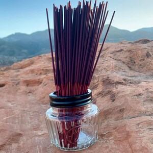 May include: A bundle of purple incense sticks in a clear glass jar with a black lid. The jar has a textured surface and the words "One Quart Made In USA" printed on the side.