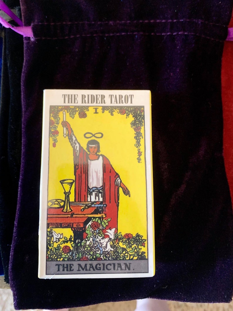 May include: The Rider Tarot card, The Magician, features a yellow background with a man in a red robe holding a wand. The card is surrounded by a border of roses and vines.
