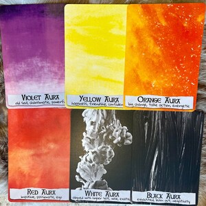 May include: Six cards with different colored backgrounds and text describing the meaning of each color aura. The colors are violet, yellow, orange, red, white, and black. The text on the cards reads: "Violet Aura: old soul, charismatic, powerful", "Yellow Aura: happiness, friendship, confident", "Orange Aura: big change, take action, energetic", "Red Aura: impulsive, passionate, ego", "White Aura: aligned with higher self, wise, exalted", and "Black Aura: exhausted, bum out, negativity".