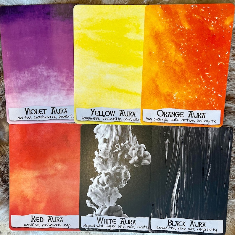 May include: Six cards with different colored backgrounds and text describing the meaning of each color aura. The colors are violet, yellow, orange, red, white, and black. The text on the cards reads: "Violet Aura: old soul, charismatic, powerful", "Yellow Aura: happiness, friendship, confident", "Orange Aura: big change, take action, energetic", "Red Aura: impulsive, passionate, ego", "White Aura: aligned with higher self, wise, exalted", and "Black Aura: exhausted, bum out, negativity".
