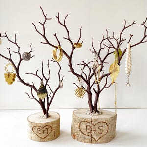 May include: Two brown jewelry display trees with various earrings, rings, and necklaces. The trees are mounted on wooden bases with carved hearts and initials. The jewelry includes gold, silver, and pearl pieces.
