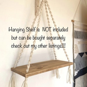 Puede incluir: Una estanter&iacute;a colgante de macram&eacute; con una repisa de madera y borlas blancas. La estanter&iacute;a est&aacute; colgada de un soporte de madera fijado a una pared. El texto "Hanging Shelf is NOT included but can be bought separately check out my other listings!!!" es visible en la imagen.