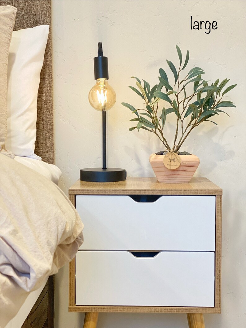 May include: A white nightstand with two drawers and wooden legs. A black lamp with a light bulb is on the nightstand. A potted plant with green leaves is on the nightstand. The word "large" is written on the wall.