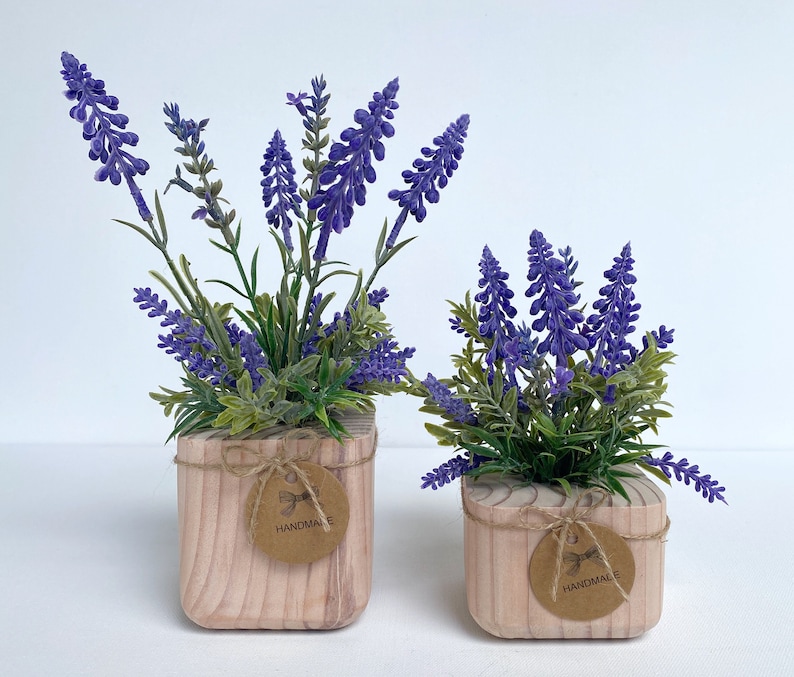 K&ouml;nnte beinhalten: Zwei Topfpflanzen mit Lavendel und lila Bl&uuml;ten in Holzt&ouml;pfen mit braunem Bastband und einem handgefertigten Etikett.