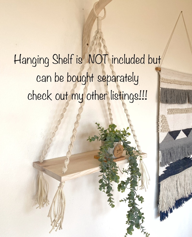 May include: A macrame plant hanger with a wooden shelf and tassels. The shelf is empty, but a potted plant is hanging from the hanger. The text "Hanging Shelf is NOT included but can be bought separately check out my other listings!!!" is visible in the image.
