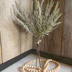 May include: A bouquet of dried, light green, artificial lavender stems with a wooden bead garland with a jute tassel.