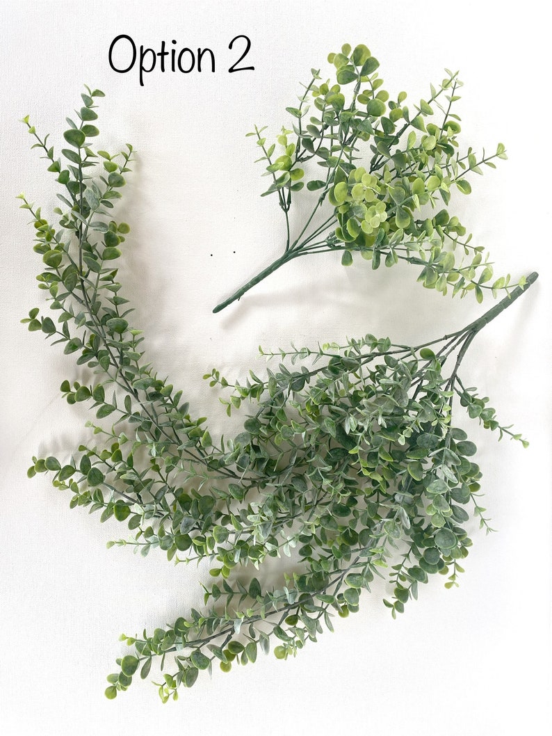 May include: Two bunches of artificial greenery, one with long trailing stems and the other with shorter stems. The greenery is a light green color and has a realistic appearance.
