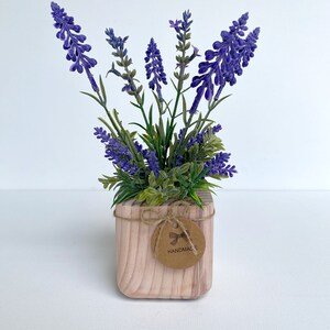 K&ouml;nnte beinhalten: Ein kleiner Holztopf mit einer lila Lavendelpflanze. Der Topf hat ein braunes Etikett mit der Aufschrift "HANDMADE".