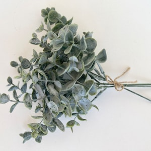 May include: A bunch of artificial eucalyptus stems with a light green and gray color, tied together with twine.