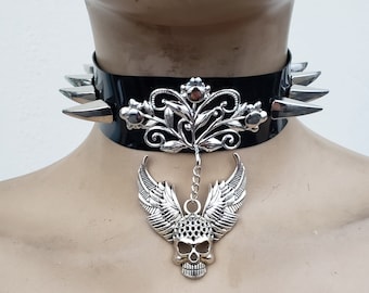 May include: Black leather choker with silver spikes and a silver skull pendant with wings. The pendant is attached to a silver chain with a floral design.