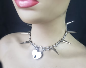 May include: Silver choker necklace featuring a heart-shaped padlock and sharp spikes. The necklace is made of metal and has a silver finish.