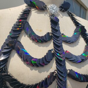 K&ouml;nnte beinhalten: Eine schwarze, schimmernde Kettenhemdkette mit einem silbernen Verschluss. Die Kette besteht aus kleinen, &uuml;berlappenden Schuppen, die einen schimmernden Effekt erzeugen.