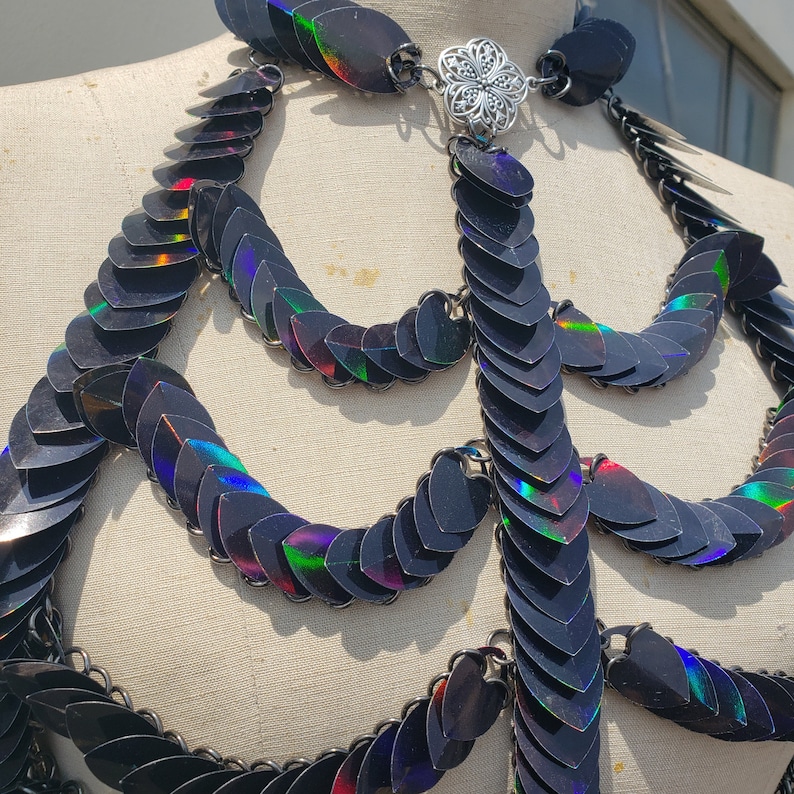 K&ouml;nnte beinhalten: Eine schwarze, schimmernde Kettenhemdkette mit einem silbernen Verschluss. Die Kette besteht aus kleinen, &uuml;berlappenden Schuppen, die einen schimmernden Effekt erzeugen.