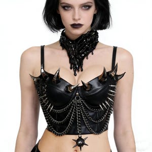 May include: Black leather corset with silver spikes and chain detailing. The corset features a pointed design and a pendant. A matching black choker with a dripping design completes the look. The overall style is gothic and edgy.