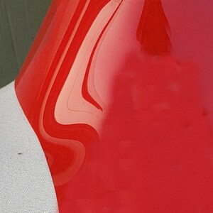 May include: A close-up of a bright red, glossy, smooth surface. The surface is curved and has a slight ripple effect.