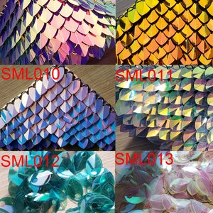 K&ouml;nnte beinhalten: Sortiment aus irisierenden, holografischen und metallischen Schuppen in verschiedenen Farben, darunter Silber, Schwarz, Rosa, Gold, Blau und Gr&uuml;n. Die Schuppen sind in Reihen und Spalten angeordnet, wobei sich einige Schuppen &uuml;berlappen. Die Schuppen sind alle ungef&auml;hr gleich gro&szlig; und gleich geformt und haben eine gl&auml;nzende, reflektierende Oberfl&auml;che.