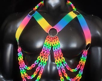Peut inclure: Harnais de poitrine arc-en-ciel avec des anneaux et des chaînes en métal argenté. Les sangles passent du rose au jaune puis au bleu. Les chaînes pendent verticalement, créant un effet superposé. Le design est vibrant et accrocheur.