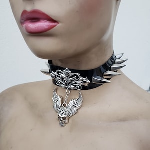May include: Black leather choker with silver spikes and a dangling skull pendant with wings. The pendant features a floral design.