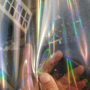 May include: A sheet of iridescent holographic vinyl with a rainbow pattern. The vinyl has a textured surface and is slightly wrinkled.