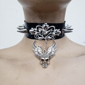 May include: A black leather choker with silver spikes and a silver skull pendant with wings and floral accents.