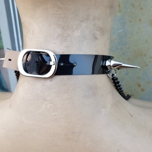 K&ouml;nnte beinhalten: Schwarzer Leder-Choker mit einer silbernen Schnalle und einem silbernen Spike, der an einer silbernen Kette befestigt ist.