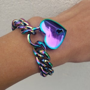 Puede incluir: Un brazalete de encanto iridiscente arcoíris con un candado en forma de corazón. El brazalete está hecho de un estilo de cadena de eslabones gruesos.