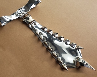 Könnte beinhalten: Ein glänzendes silbernes Metallaccessoire mit einer Reihe dreieckiger Spitzen entlang einer Kante. Das Accessoire hat eine Schnalle und einen Riemen an einem Ende und eine spitze Spitze am anderen. Das Metall reflektiert das Licht und erzeugt ein helles, auffälliges Aussehen.