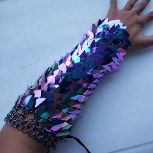 Op de afbeelding: Een metalen armband met schitterende paarse en blauwe schubben. De armband is gemaakt van overlappende schubben die zijn bevestigd aan een kettingmailbasis.