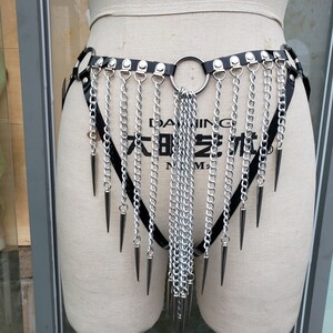 May include: A black leather harness with silver chains and spikes. The harness has a large silver ring in the center and is decorated with small silver studs.