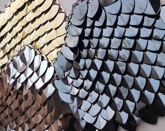 Könnte beinhalten: Zwei dekorative Kettenhemden aus Metall, eines golden und eines silbern, mit einem schuppigen Muster.