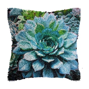 May include: Square throw pillow featuring a detailed, textured design of a succulent plant. The pillow showcases shades of blue, green, and white, with a dark border. The design is reminiscent of a rug or textile art.