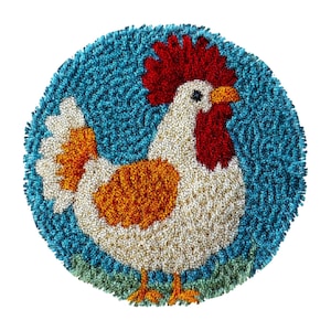 May include: A round, handmade rug featuring a rooster design. The rooster has a red comb, orange and white body, and is set against a blue background. The rug is made of textured yarn and has a green border at the bottom.