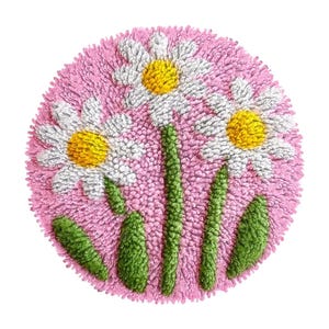 Könnte beinhalten: Ein runder, rosa getufteter Teppich mit drei weißen Gänseblümchen mit gelben Zentren und grünen Stielen und Blättern. Der Teppich hat ein strukturiertes Aussehen, wobei sich die Blumen und Blätter vom rosa Hintergrund abheben. Das Design ist ein Blumendesign.