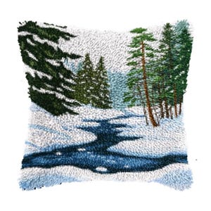 May include: A square, textured cushion depicting a winter landscape. The design shows a snow-covered area, a dark blue river, and evergreen trees in shades of green and brown. The cushion has a white background.