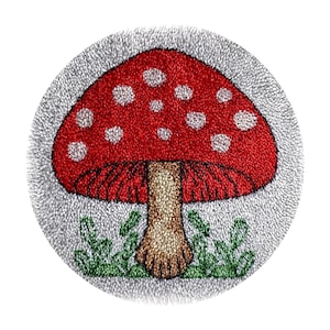 Könnte beinhalten: Ein runder, strukturierter Teppich mit einem roten Pilz mit weißen Punkten. Der Pilz hat einen braunen Stiel, grünes Gras und einen grauen Rand. Der Teppich ist wahrscheinlich handgefertigt und für die Inneneinrichtung geeignet. Durchmesser ca. 30 cm.