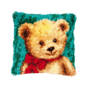 Puede incluir: Una almohada de peluche con un oso de peluche marrón que lleva una pajarita roja sobre un fondo verde turquesa.