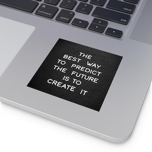 May include: A black sticker with white text that reads "THE BEST WAY TO PREDICT THE FUTURE IS TO CREATE IT." The sticker is on a silver laptop.